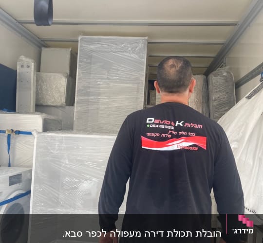 אדם עומד במשאית עם רהיטים עטופים בניילון